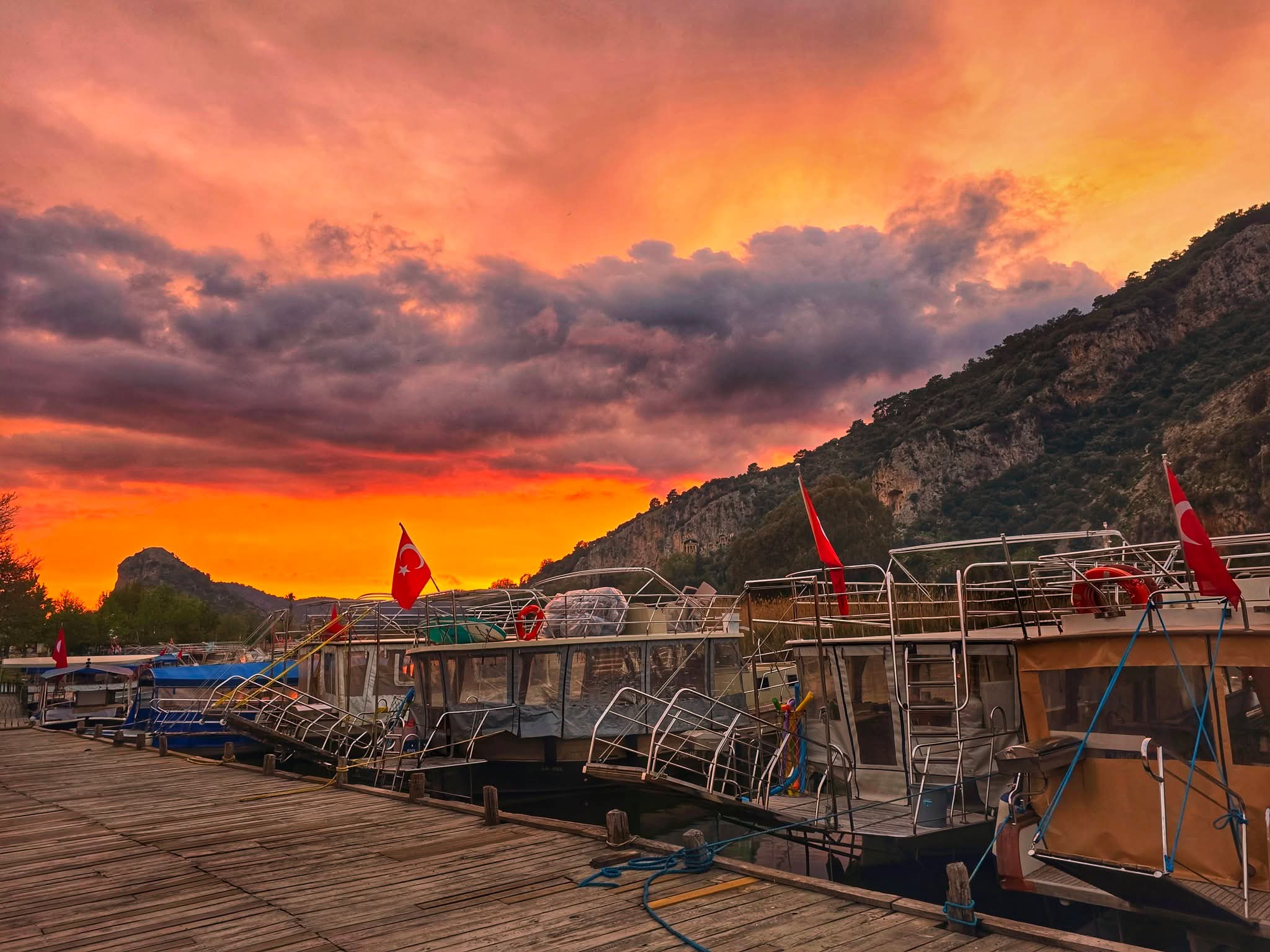 Tour boats moored at the Dalyan jetty at sunset with the rock cliff behind